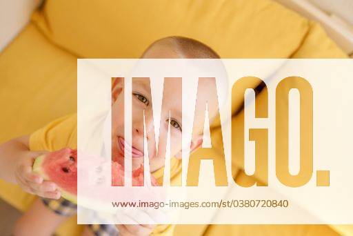 A closeup of a male child eating watermelon on a yellow couch 623215 ,model released, Symbolfoto RECORD DATE NOT STATED