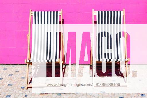 Black and white striped sun loungers against pink tile background 1948841