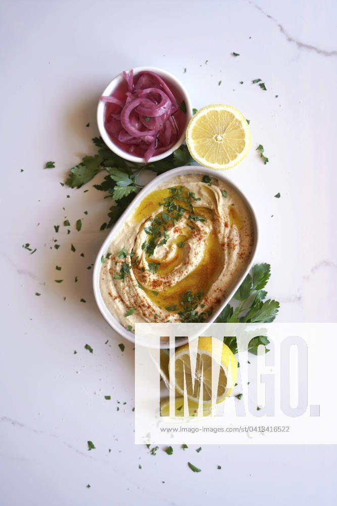 Chickpea hummus served with olive oil, pickled red onion, lemons, and flatbread on a white marble table background. Minimal layout flatlay. Chickpea hummus served with olive oil, pickled red onion, lemons, and flatbread on a white marble table background. Minimal layout flatlay.