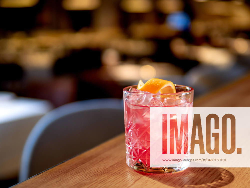 Transparent pink alcohol cocktail, vodka gin-tonic Transparent pink alcohol cocktail with ice, aperol and gin on bar counter in restaurant interior. Alcohol cocktail decorated orange zest spiral. Cold alcoholic cocktail in bar or nightclub. Copy space