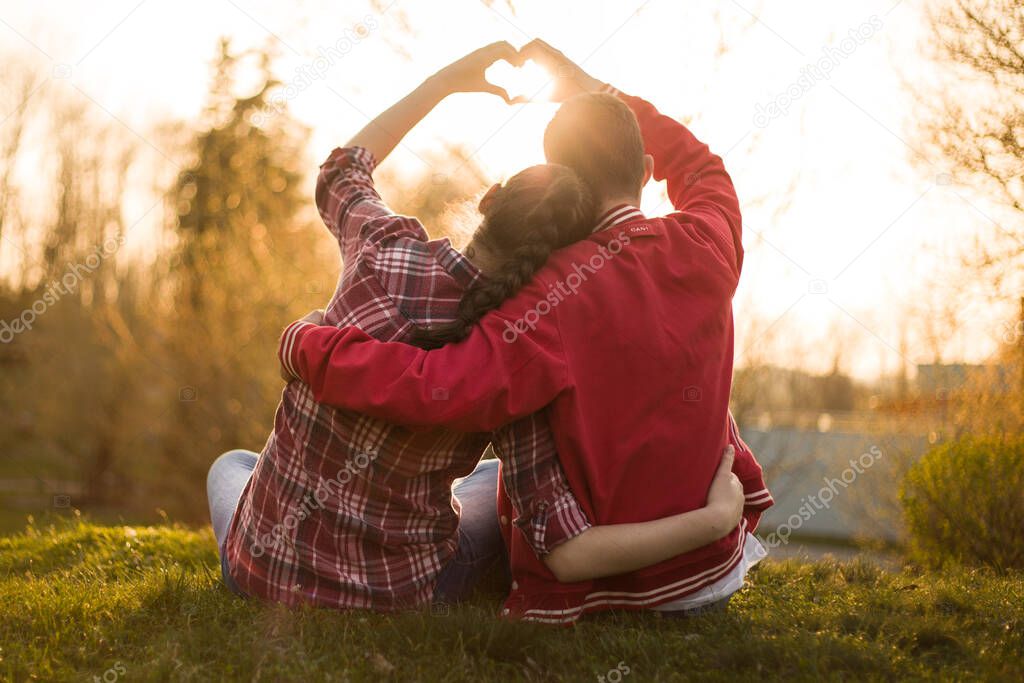 Beautiful relationship between boy and girl, women and men. Love is in the air. They are in love. I love you. Two persons showing heart by hands in amazing summer sunset warm light.