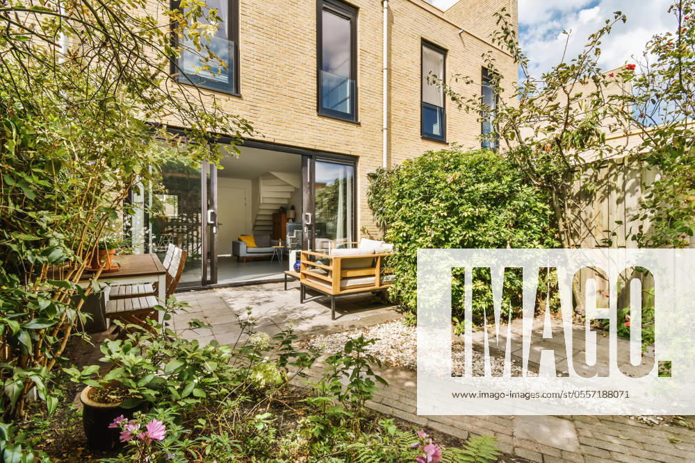 Elegant backyard patio of a modern home featuring stylish outdoor furniture, open sliding doors, and a vibrant garden. Model Released ProCreators_ID5188_167283_012