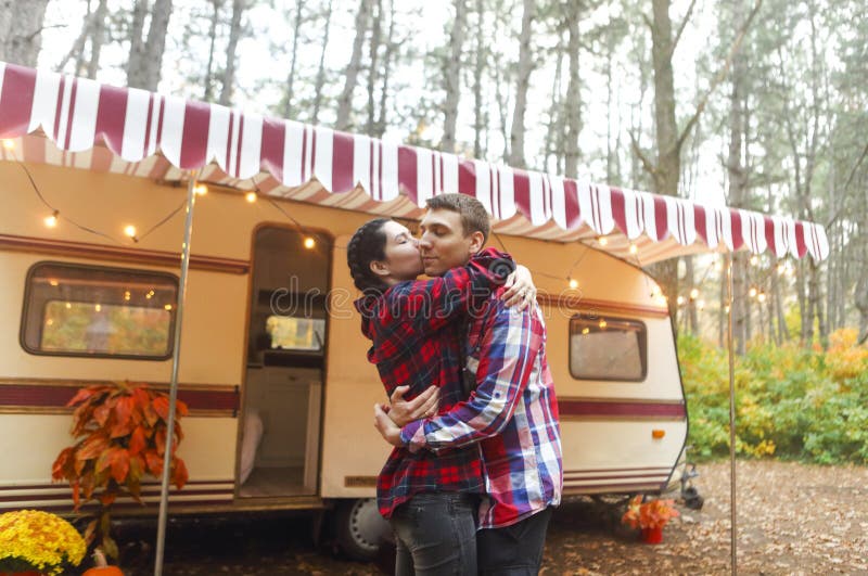 Portrait of romantic couple smiling while holding hands near house on wheels outdoors, Portrait of romantic couple man and woman smiling while hugging near house on wheels outdoors