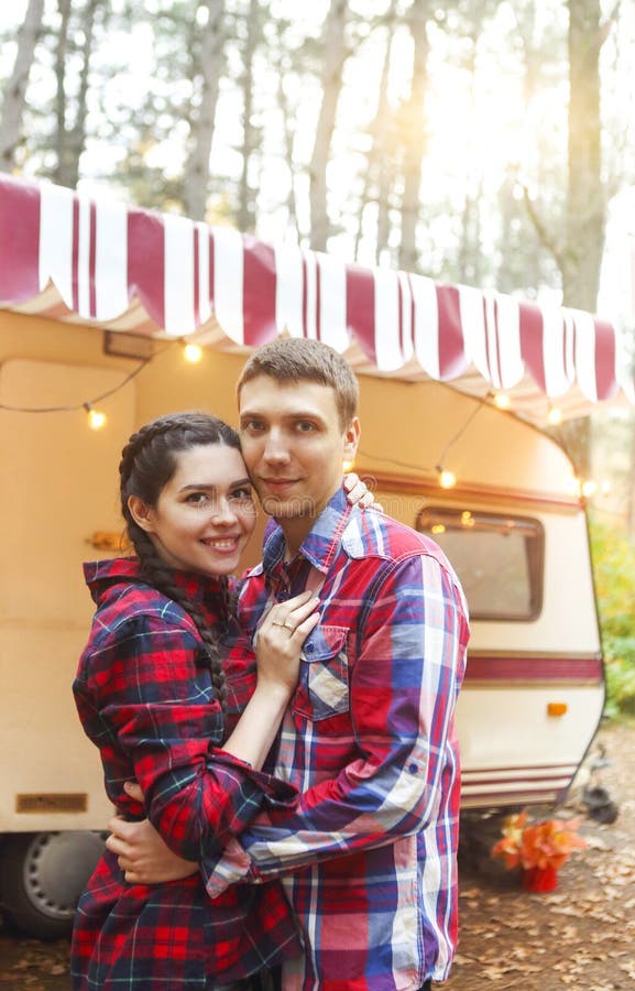Portrait of romantic couple smiling while holding hands near house on wheels outdoors, Portrait of romantic couple man and woman smiling while hugging near house on wheels outdoors