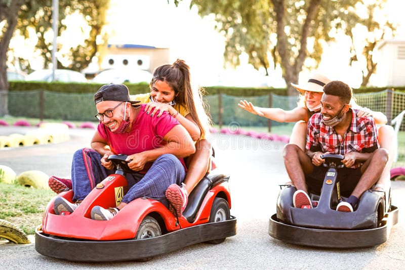 Group of multiracial friends having fun with go kart - Young people with face mask on smiling and cheerful at mini car racing -, Multiethnic friends in holiday - covid 19 times