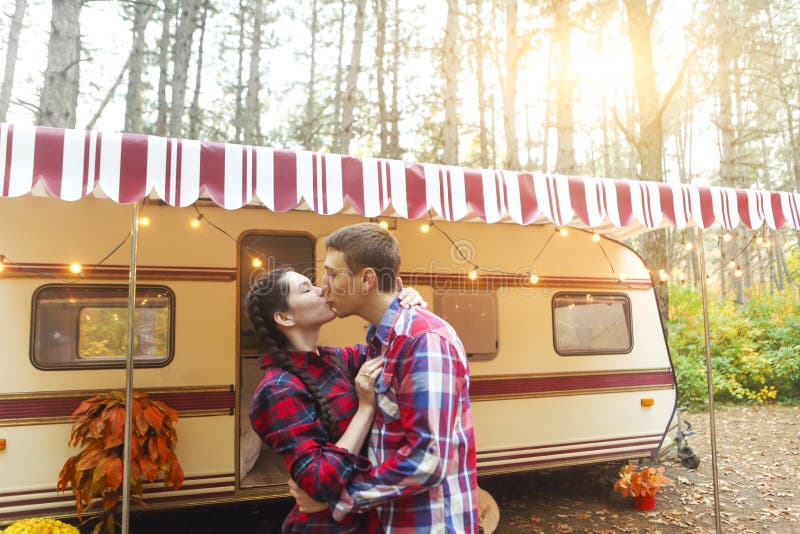 Portrait of romantic couple smiling while holding hands near house on wheels outdoors, Portrait of romantic couple man and woman smiling while hugging near house on wheels outdoors