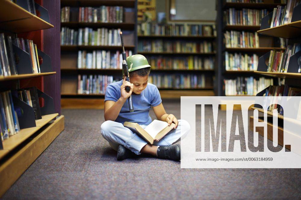 Boy with helmet and gun reading book in library model released Symbolfoto property released ZEF000195