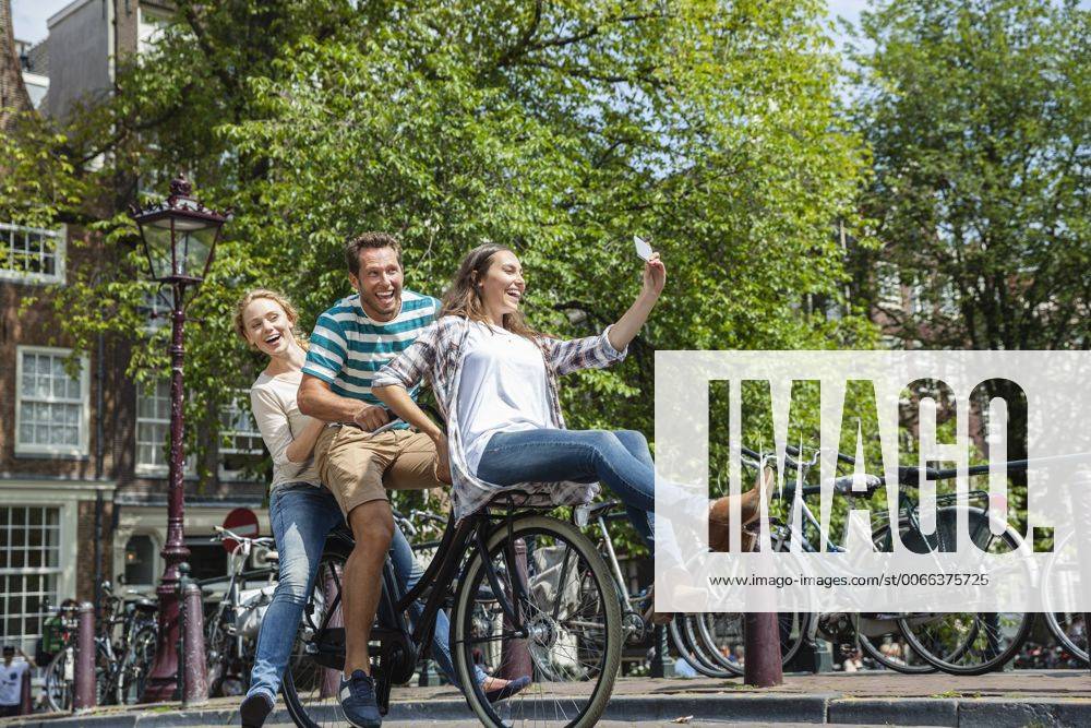 Netherlands, Amsterdam, three playful friends riding on one bicycle in the city model released Symbolfoto FMKF002146
