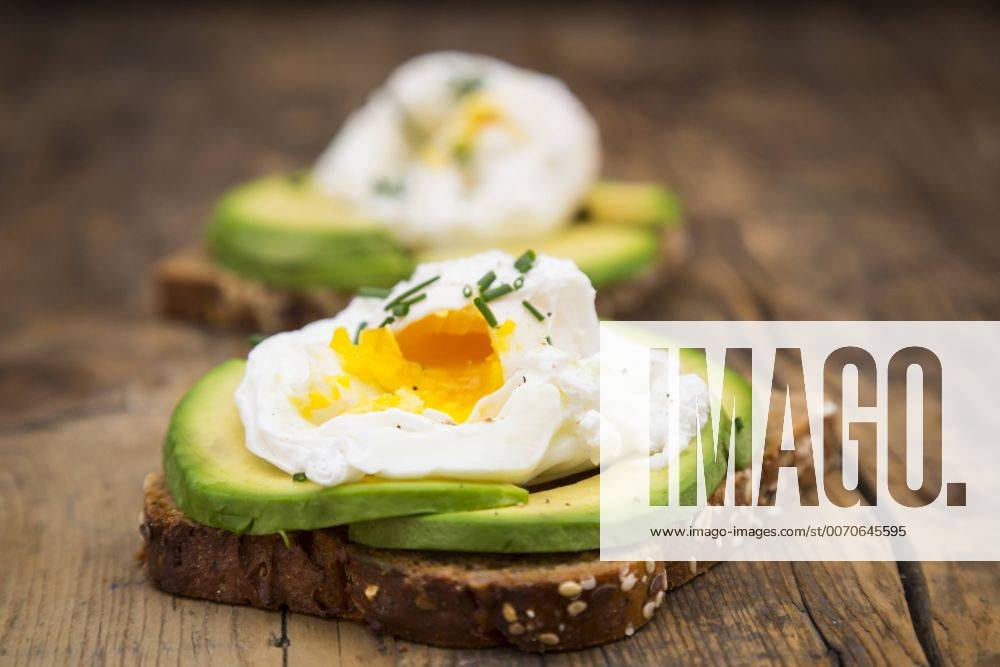 Wholemeal bread slices with sliced avocado and poached eggs on wood LVF004673