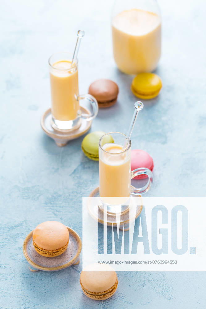 Verschiedene köstliche französische Macarons mit Eierlikör oder Eierlikör auf blauem Hintergrund Assorted delicious French macarons with egg liqueur or eggnog on blue background