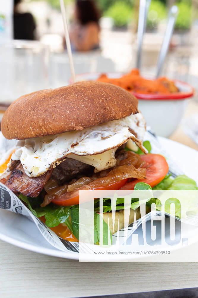 A delicious gourmet burger featuring a succulent beef patty topped with crispy bacon, a perfectly fried egg, fresh lettuce, ripe tomato slices, and vibrant greens, served on a toasted bun Model Released Gaorstudio_ID23796_690703_003