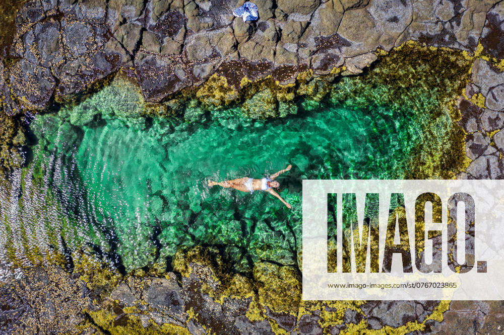 Carefree woman in bikini floating in beautiful rock pool summer Australia A woman relaxes in a beautiful seaside rock pool with sandy bottom and edged in a yellow seaweed called Neptunes necklace, Hormosira banksia ,model released, Symbolfoto