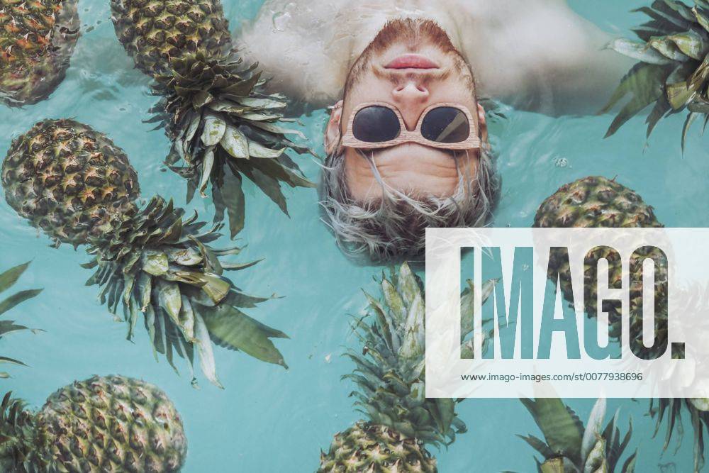 Young man in swiming pool surrounded by pineapples model released Symbolfoto RTBF00747