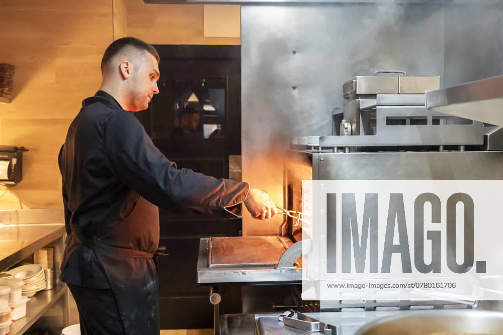 An expert chef serving meals in the bustling kitchen of a restaurant, surrounded by steam due to the use of the grill in the kitchen Model Released PaulaBerezo_ID24490_709733_007