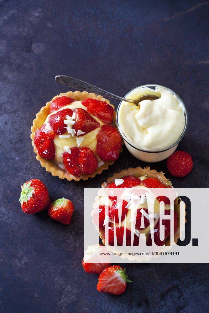 Two strawberry tartlets with custard and white chocolate shaving on dark ground CSF28581