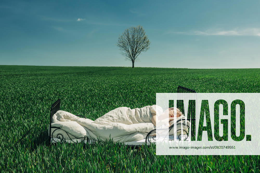 Woman sleeping in a bed in a green field under a blue sky with a lone tree in the background model released, Symbolfoto, VSNF03150