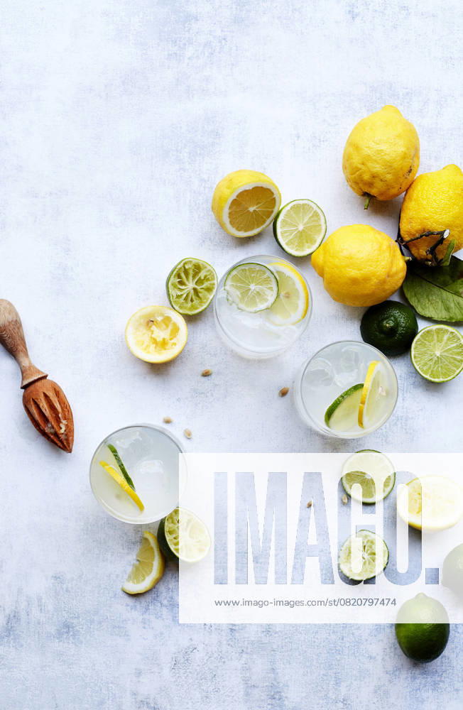 Top view of refreshing summer drinks with slices of lemon and lime on a textured white background. Wood citrus squeezer and scattered seeds add rustic charm. Model Released GeorgiaGold_ID28580_843685_002