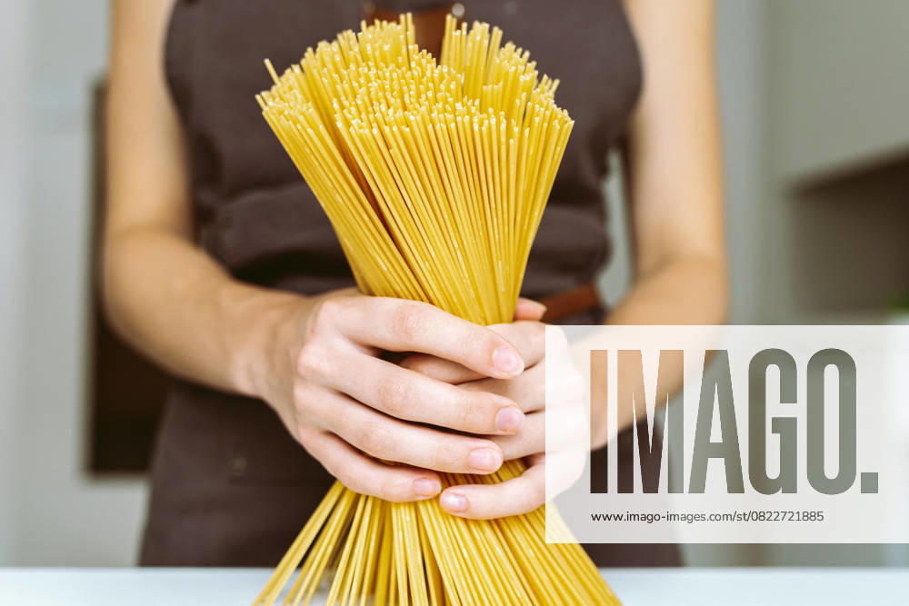 Koch mit Spaghetti in der Hand Woman in brown chef s apron holding spaghetti close-up. Chef holding spaghetti (License=RF) ,model released, Symbolfoto