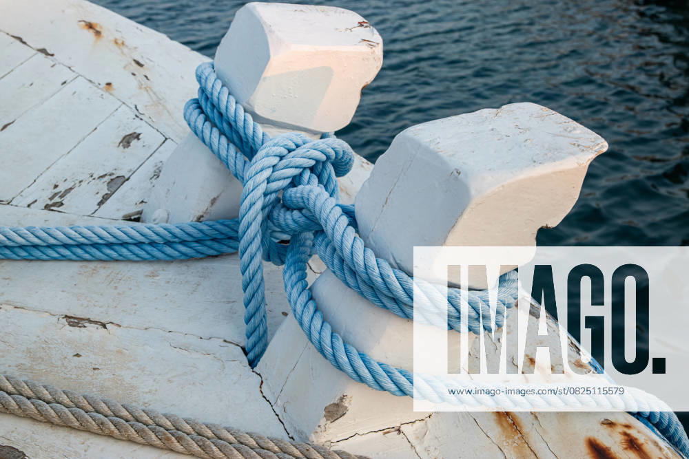 Mit einem nautischen Knoten gebundene Festmacher Close-up of blue mooring ropes tied in a nautical knot around white wooden bollards on a vintage boat (License=RF)