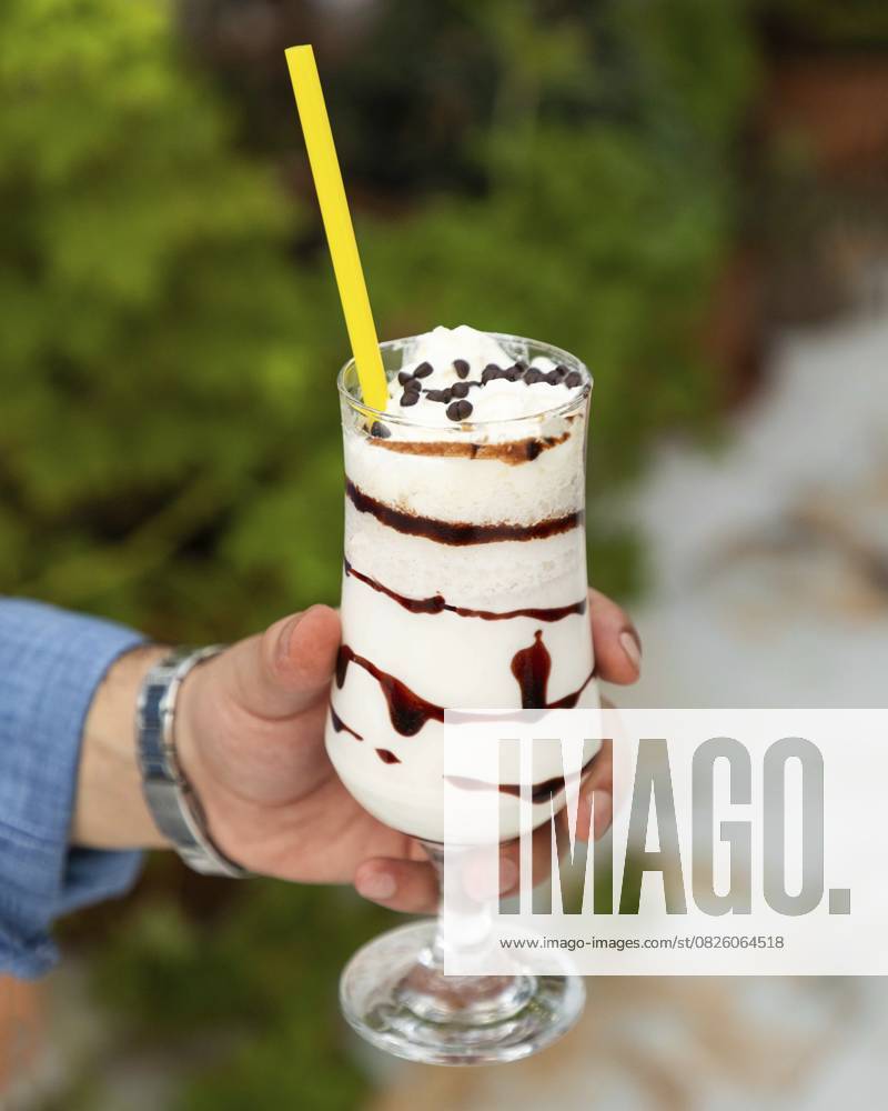IMAGO Creative, Food, Trend, Iced Coffee Der Barista hält einen erfrischenden Eiskaffee Milchshake mit Schlagsahne, Schokoladensirup und Schokoladenstückchen in der Hand Barista holding a refreshing iced coffee milkshake topped with whipped cream, chocolate syrup, and chocolate chips