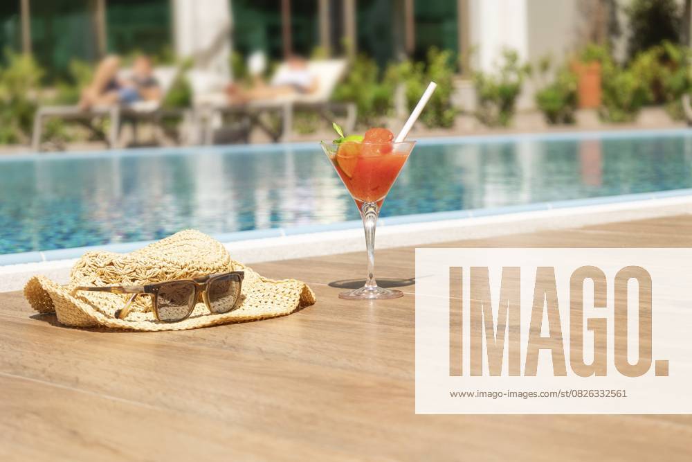 Frischer roter Cocktail mit Eis im Glas, Strandhut und Sonnenbrille am Swimmingpool. Tropischer Saft auf Luxus Urlaub. Konzept Sommerurlaub und Reisen Fresh red cocktail with ice in glass, beach hat and sunglasses on swimming pool. Tropical juice on luxury vacations. Concept summer holiday and travel.