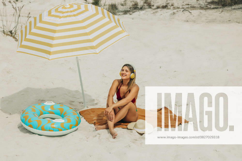 Brunette relaxing on sandy beach under umbrella with inflatable ring model released, Symbolfoto, VSNF03672
