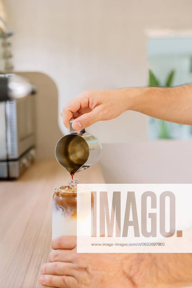 IMAGO Creative, Food, Trend, Iced Coffee PR_ID30758_11598_RandaStudio.jpg, MR_ID30758_22173_ClarenaSalamanca.jpg, MR_ID30758_22174_JorgeEnrriqueParrado.jpg, MR_ID30758_22175_LilianaAndreaLonga.jpg A person skillfully pours espresso over ice and milk in a glass, crafting a refreshing iced latte in a bright, modern kitchen. The setting is cozy and inviting, Property released Model Released AngelaRober_ID30758_1041723_022