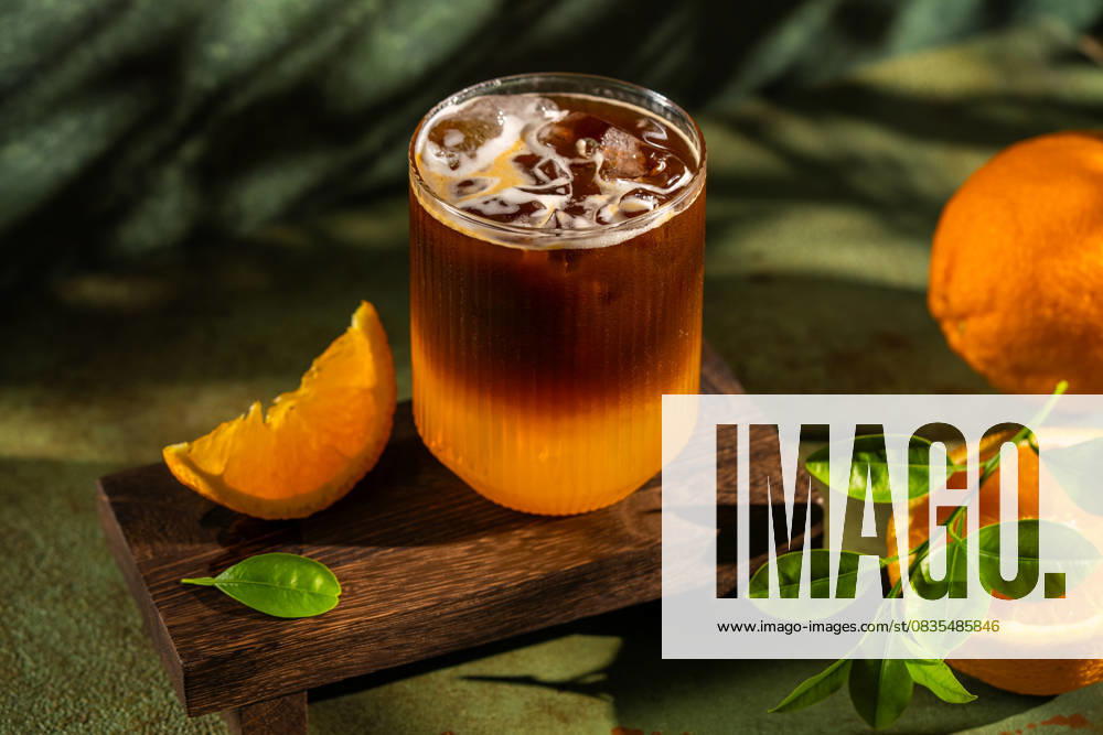 IMAGO Creative, Food, Trend, Iced Coffee Iced coffee with fresh orange slice on wooden board Refreshing iced coffee served in a textured glass on a wooden board, accompanied by a fresh orange slice. Perfect for a summer day with vibrant greenery and natural light Model Released Ellsy_ID31375_1067228_007