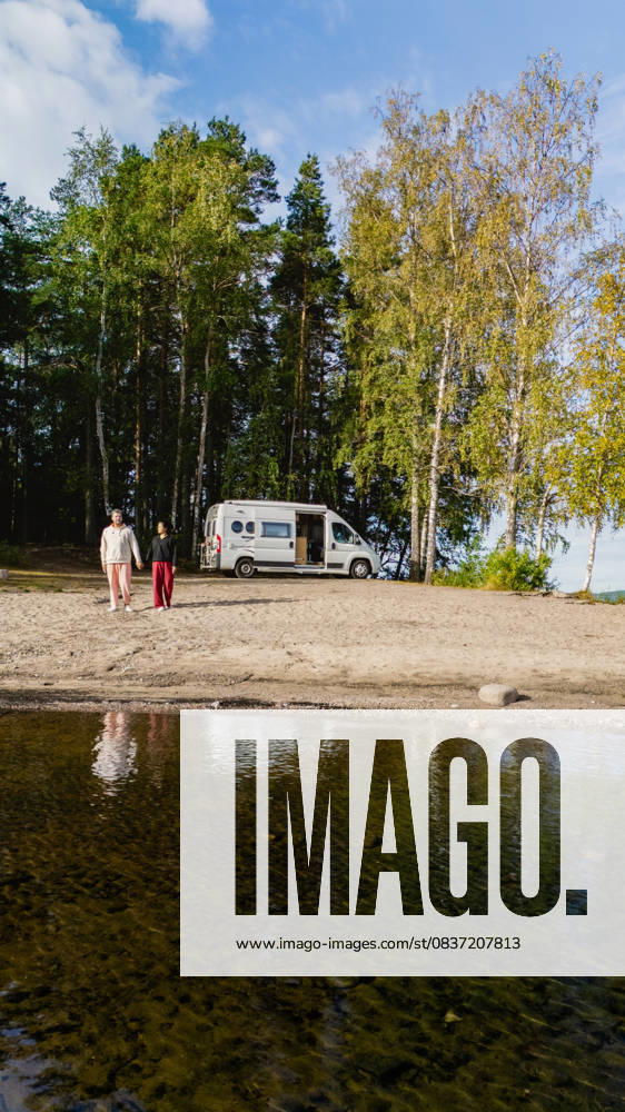 Einen ruhigen Tag am Saimaa-See in Finnland mit einem Wohnmobil und der Natur genießen Two individuals stroll along the sandy shore of Lake Saimaa in Finland, with a camper van parked nearby. Vibrant greenery surrounds the serene waters, creating a tranquil atmosphere. (License=RF) ,model released, Symbolfoto