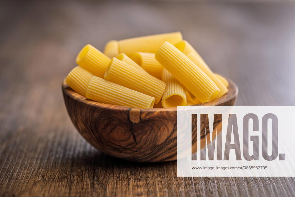 Ungekochte Rigatoni-Nudeln in einer Schüssel auf einem Holztisch. Uncooked rigatoni pasta in bowl on a wooden table. (License=RF)
