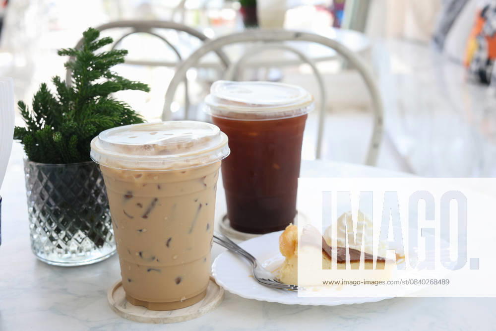IMAGO Creative, Food, Trend, Iced Coffee Zwei Eiskaffees und ein Stück Kuchen auf einem Tisch mit unscharfem Hintergrund. Two iced coffees and a slice of cake on a table blurred background. (License=RM)