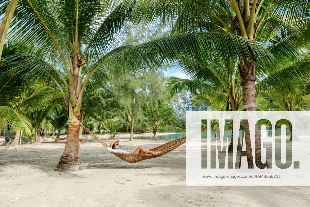Entspannen in einer Hängematte umgeben von üppigen Palmen auf der Insel Koh Kood in Thailand A peaceful scene of an Asian woman lounging in a hammock beneath tall palm trees on Koh Kood Island. Soft sandy beach and tranquil water create a tropical paradise in Thailand. (License=RF) ,model released, Symbolfoto