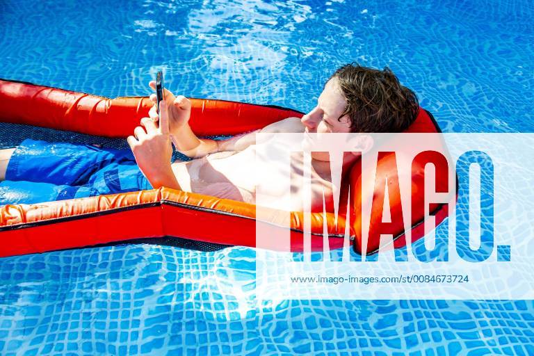 Boy floating on water in swimming pool using smartphone model released Symbolfoto SARF03780