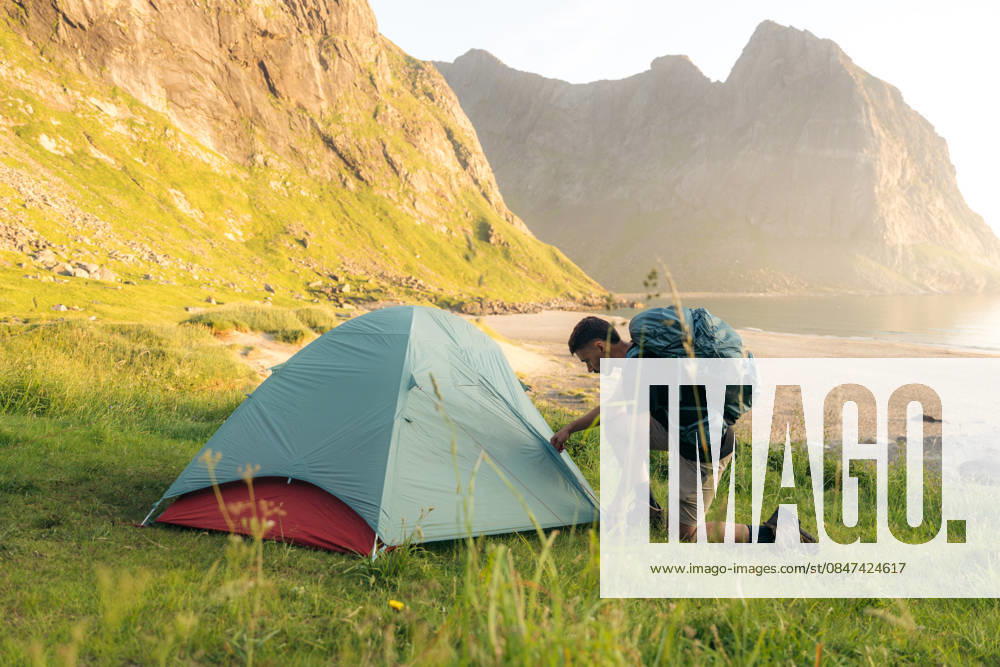 MR_ID32524_23616_IoritzLopez.jpg, MR_ID32524_23617_ArgineSatrustegui.jpg A hiker sets up a tent in the stunning Lofoten Islands, surrounded by majestic mountains and serene beaches, capturing the essence of a thrilling camping adventure. Model Released IoritzLopez_ID32524_1108276_058