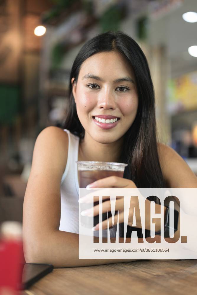 IMAGO Creative, Food, Trend, Iced Coffee Junge schöne asiatische Frau sitzt und trinkt Eiskaffee im Restaurant Young beautiful Asian woman sitting and drinking iced coffee at restaurant