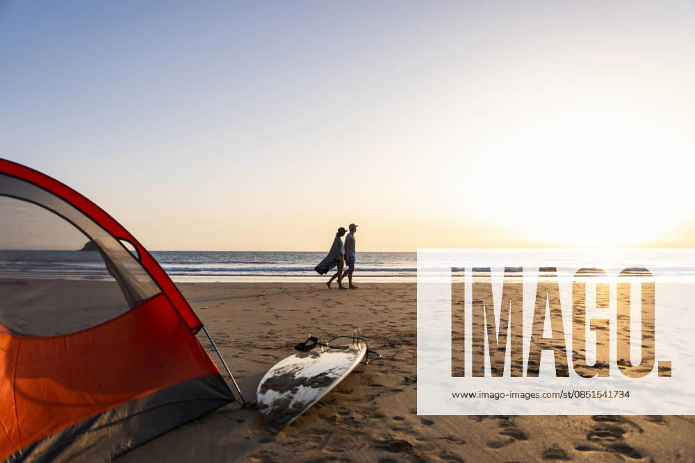 Couple walking with surfboard by tent on beach at sunset model released, Symbolfoto, UUF36535