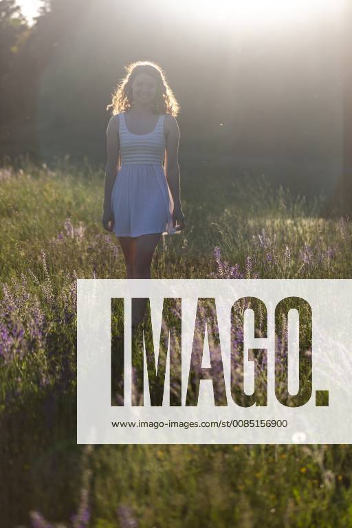 IMAGO Creative: Sommer, Abendspaziergang Young woman walking on flower meadow in the evening light model released Symbolfoto SARF03810