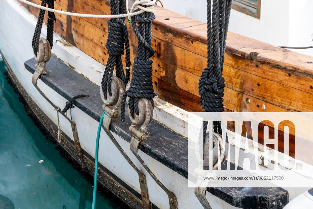 Details zu Takelage und Knoten historischer Segelschiffe Cartagena, Murcia - Spain - 01-16-2024: Close-up of traditional sailing ship s rigging, featuring knotted ropes, wooden deadeyes, and taut steel cables against wooden hull (License=RF)