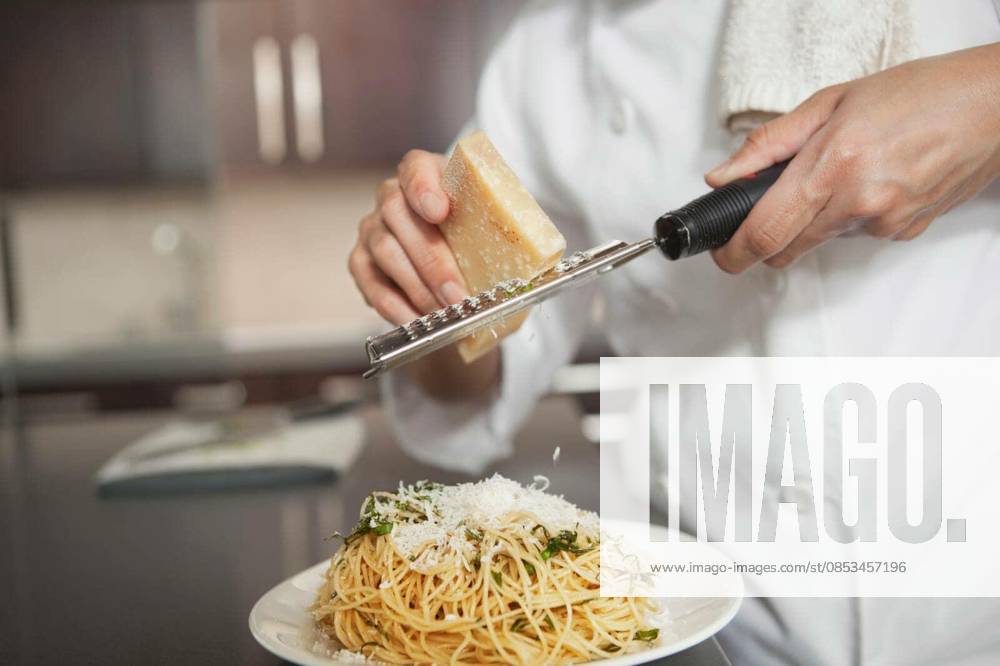 Chef Grating Cheese Onto Pasta In Kitchen - Midsection of female chef grating cheese onto pasta in kitchen model released Symbolfoto