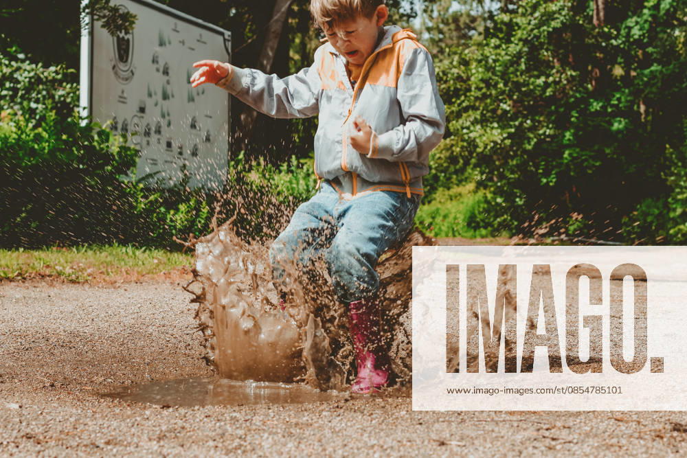 Ein fröhliches Kind springt in wasserdichten Stiefeln durch eine Pfütze. Ein Junge, der voller Spritzwasser ist, spielt in einem herbstlichen Park. A happy child jumps in a puddle in waterproof boots. A boy with splashes is playing in an autumn park. Outdoor activities in rainy weather (License=RF) ,model released, Symbolfoto