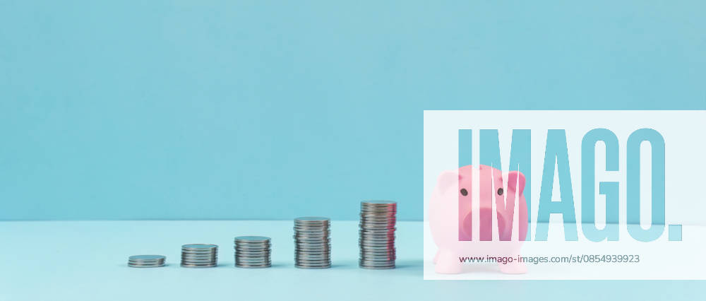 Sparschwein mit aufgestapelten Münzen auf blauem Hintergrund A pink piggy bank placed next to stacks of coins against a blue background, symbolizing financial savings and growth. (License=RF)