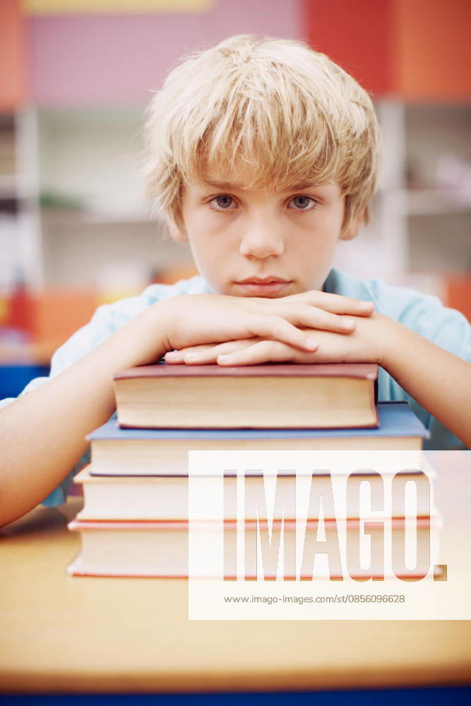 I cant believe I have to read this much. A serious young boy sitting at his desk and leaning his chin on a stack of books (License=RF) ,model released, Symbolfoto