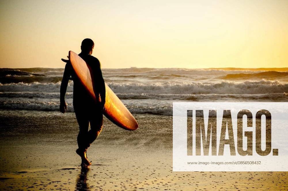 Surfer walking on the beach with the waves at sunset in Portugal. model released Symbolfoto