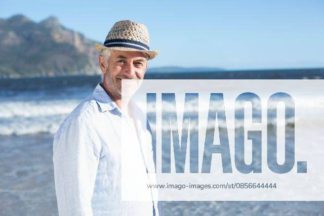 Man standing in shallow water at sandy beach wearing linen shirt and straw hat, looking, model released, 03.04.2014 06:00:00, 8079340