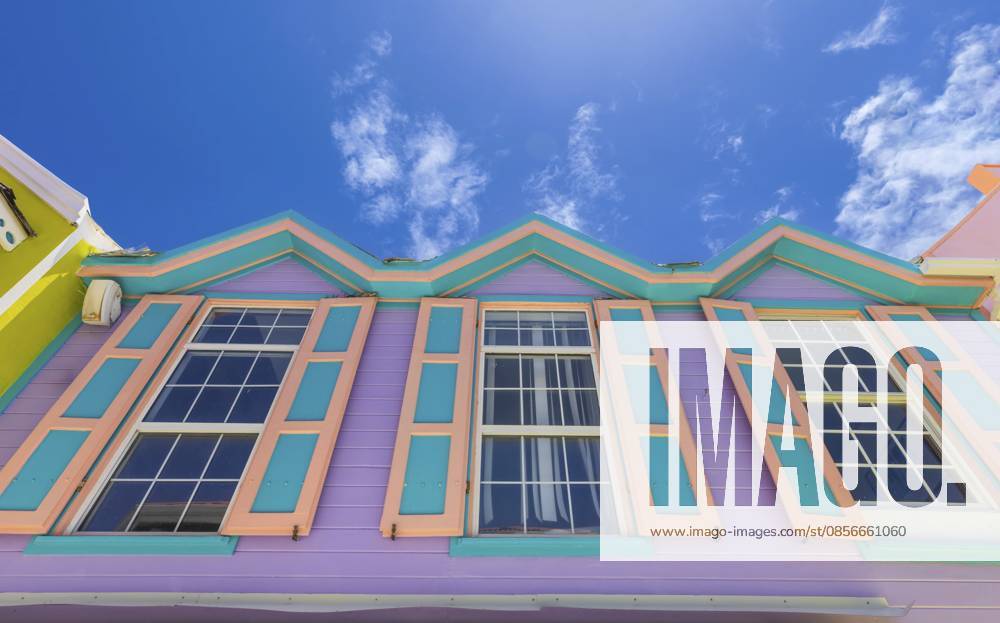 Niedrigansicht eines lebendigen lila und türkisfarbenen Kolonialgebäudes mit dekorativer Zickzack Dachlinie und blaugrünen Fensterrahmen in Philipsburg, Sint Maarten, vor einem strahlend blauen Himmel Low angle view of a vibrant purple and turquoise colonial building with decorative zigzag roofline and teal window frames in Philipsburg, Sint Maarten, against a bright blue sky