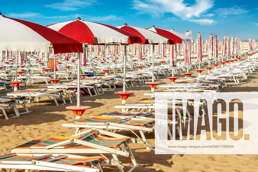 Red and white umbrellas and sunlongers on the sandy beach in Italy