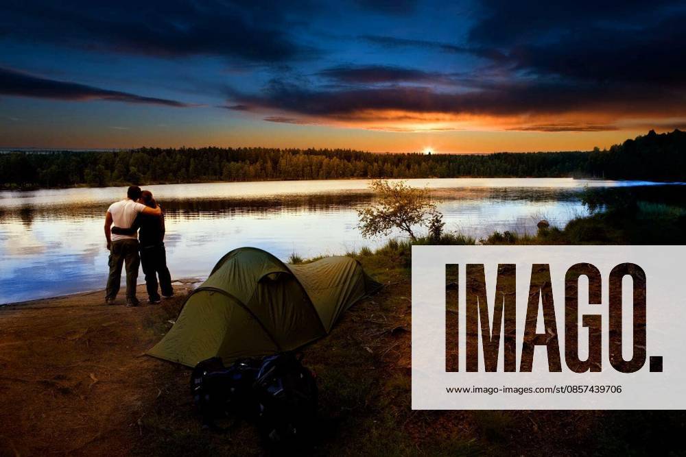 A pair of campers with a tent set against a beautiful sunset lake landscape model released Symbolfoto