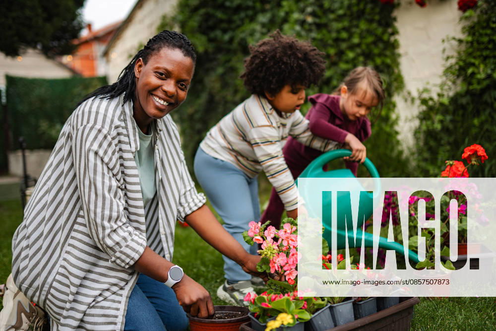 Mutter und Kinder pflanzen Blumen im Garten hinter dem Haus Smiling woman and two kids working together in garden, planting and watering flowers (License=RF) ,model released, Symbolfoto