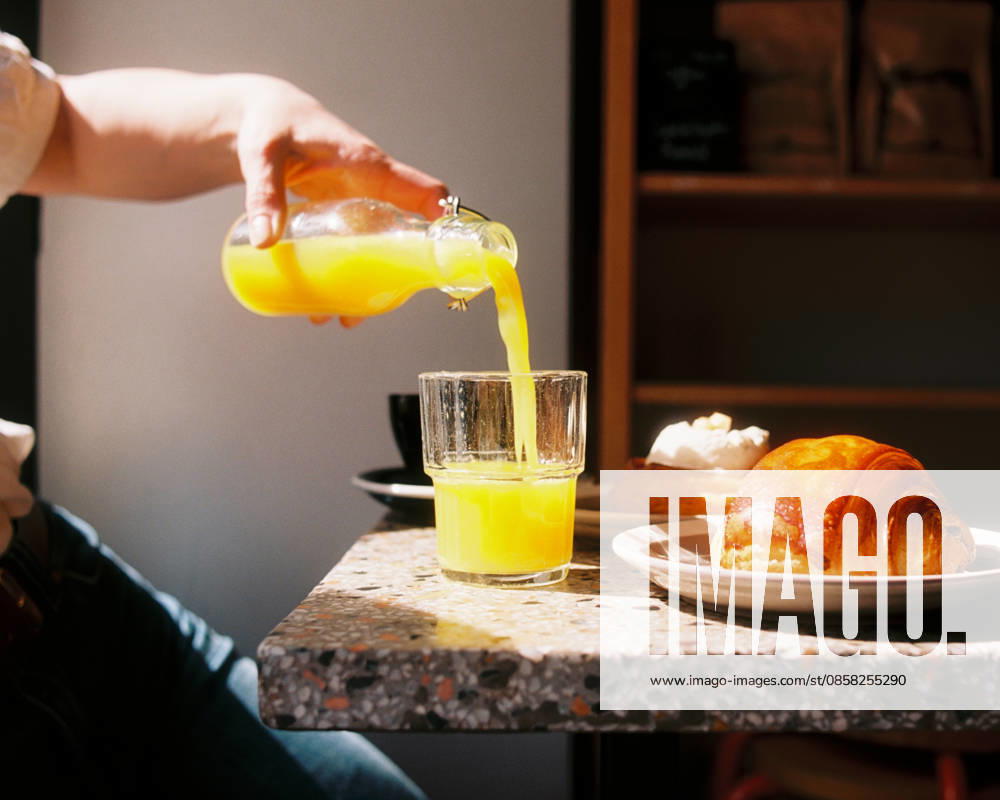 Hand pouring orange juice at sunny cafe breakfast Stockholm, Stockholm County, Sweden R_RABE260602-2038653-01 ,model released, Symbolfoto