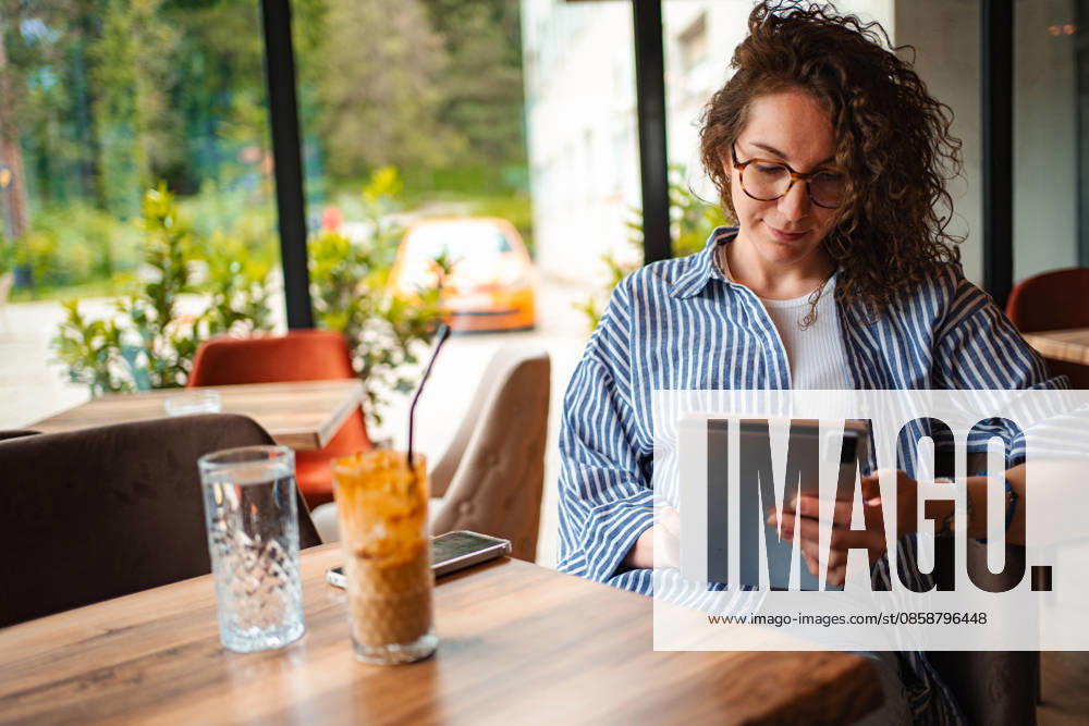 IMAGO Creative, Food, Trend, Iced Coffee Frau, die in einem Café mit einem Tablet im Homeoffice arbeitet Woman using tablet computer in cafe, enjoying iced coffee during work break (License=RF) ,model released, Symbolfoto